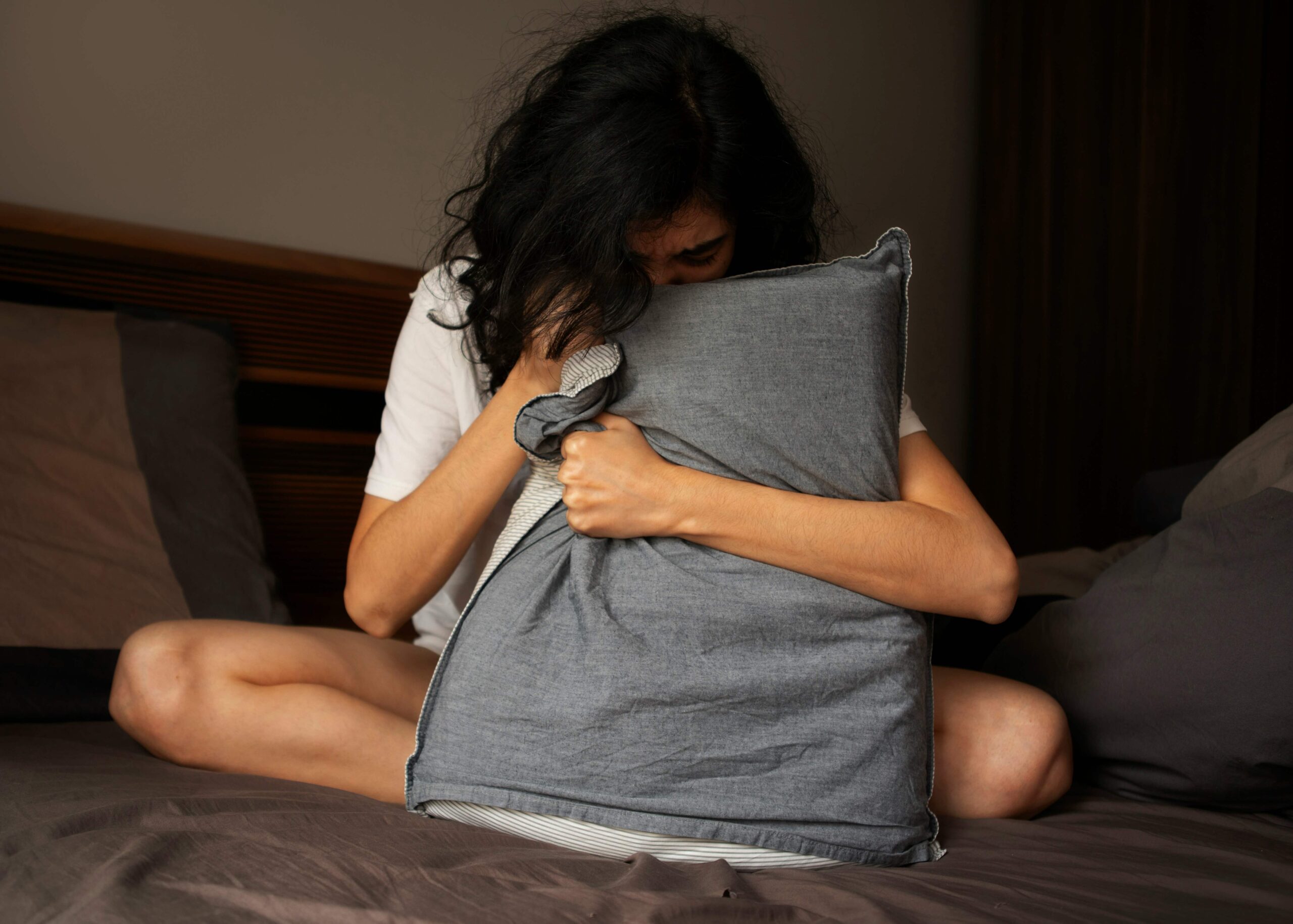 a woman is sitting on the bed, holding a pillow and seems annoyed as she couldn't sleep